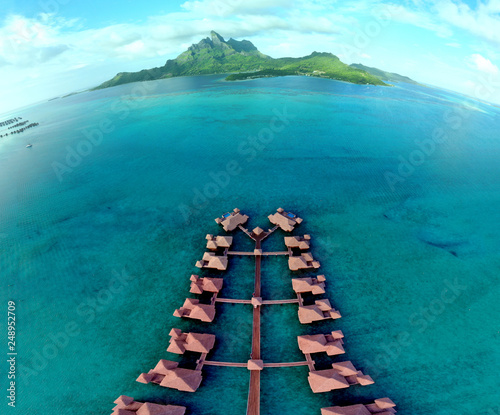 Aerial view of overwater bungalow villas with thatched roofs in the Bora Bora lagoon in French Polynesia