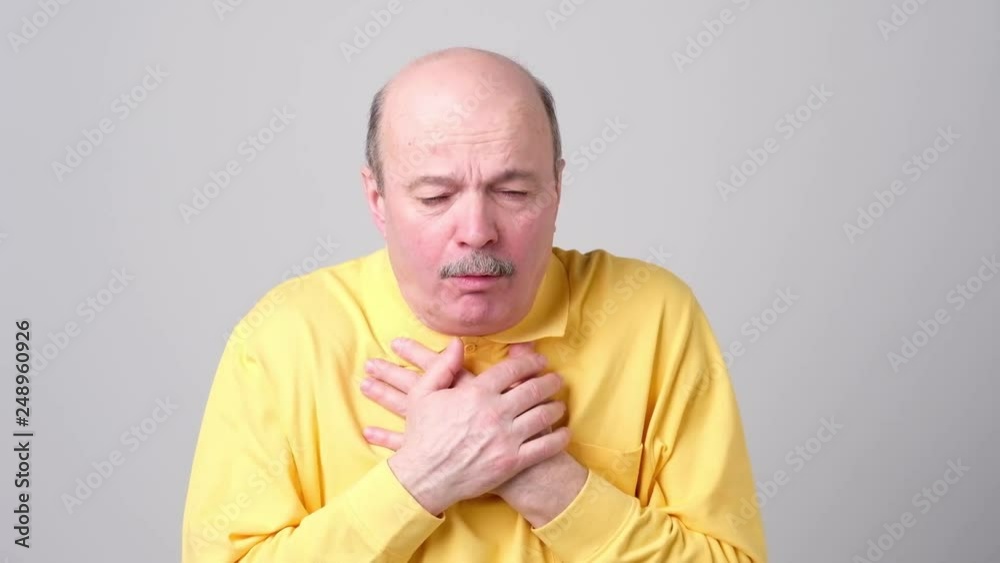 Mature hispanic man in yellow t-shirt man coughing being ill. Mature hispanic man in yellow t-shirt man coughing being ill.