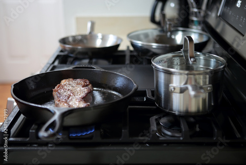 New York strip steak frying in a cast iron pan on a natural gas stove top.