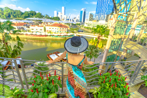 Canvas Print Tourist woman with wide hat looking panorama from terrace over Clarke Quay and Riverside area in Singapore, Southeast Asia