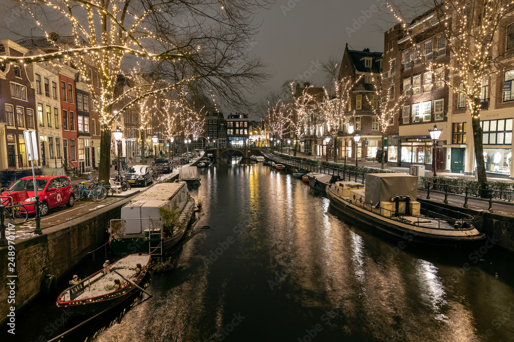 AMSTERDAM, NETHERLANDS - JANUARY 23, 2019: illuminated trees and buildings reflected in water in december by night, Amsterdam, Netherlands
