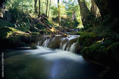 Fototapeta Naklejka Na Ścianę i Meble -  Long exposure of a river creek with a small waterfall. Sunset and strong detail bokeh view. blue calm warm water