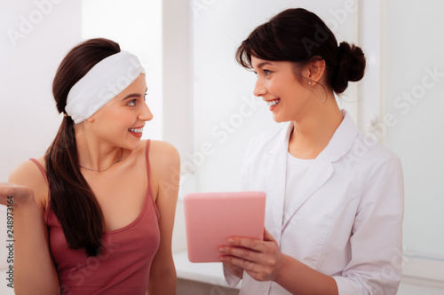 Positive friendly female cosmetologist holding a tablet