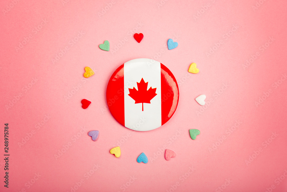 Happy Canada Day greeting card with Canadian flag in centre middle and many colorful candies hearts around it on living coral pink background. Multiculturalism national values concept.
