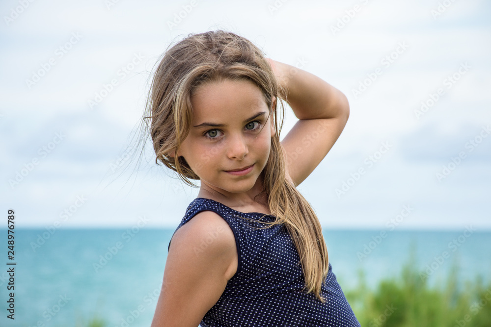 Criança modelo sentada em frente ao mar azul Criança modelo sentada em frente ao mar azul