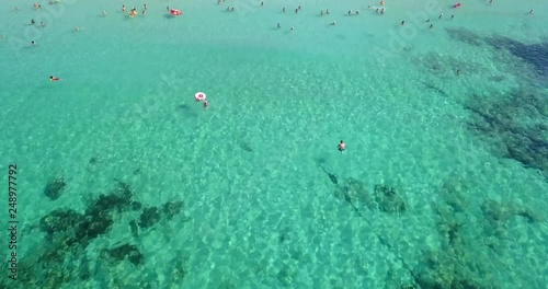 Aerial shot of tourists bathing on a sandy beach. Camera tilts up from the blue sea to reveal the beach with beach beds and beach umbrellas. photo