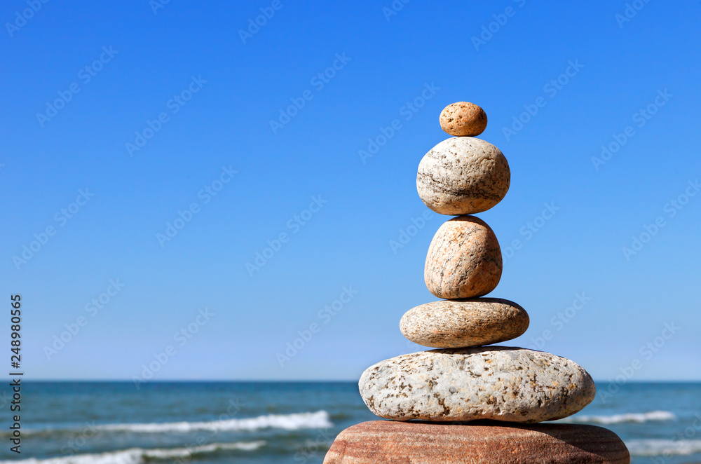 Fototapeta premium Rock zen pyramid of gray pebbles on a background of blue sky and sea.