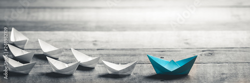 Valokuvatapetti Blue Paper Boat Leading A Fleet Of Small White Boats On Wooden Table With Vintag