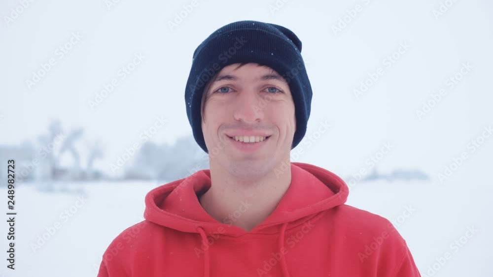 Portrait of young man in black cap look camera smiling in winter snowy cold outdoors Portrait of young man in black cap look camera smiling in winter snowy cold outdoors
