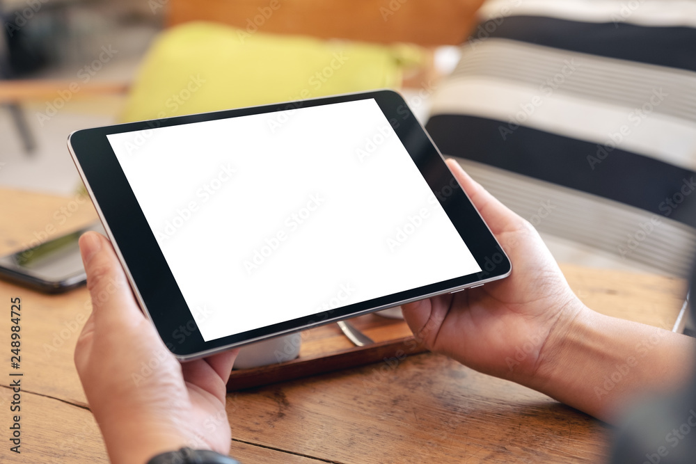 Mockup image of woman's hands holding black tablet pc with blank screen on wooden table in cafe Mockup image of woman's hands holding black tablet pc with blank screen on wooden table in cafe