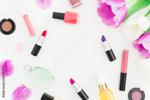 Frame made of tulips flowers and cosmetics, lipstick with nail polish on white background. Top view. Flat lay