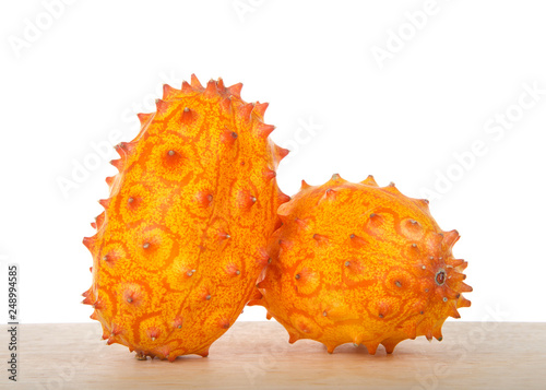 Two whole Kiwano fruit, also known as Cucumis metuliferus, horned melon, or African horned cucumber sitting on wood table isolated on white. Kiwano is a traditional food plant in Africa.