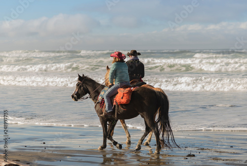 Two horses being ridden on the oregon coast on a beauty, cold, sunny day,.