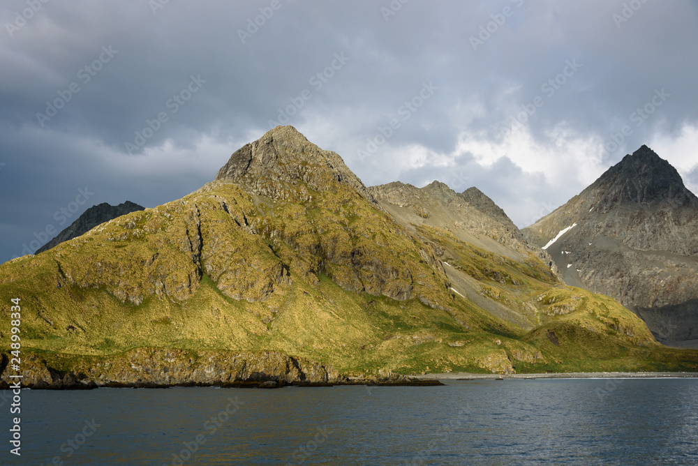 Dramatic island mountain landscape with sun beams, water, and cloudy sky, Coopers Bay, South Georgia Islands