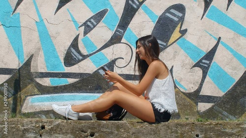 Pretty young woman taking selfie with a smart phone, wall with Graphites in the background.Slow motion 75fps photo