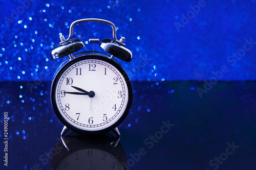 Alarm clock on a blue background, bokeh effect. Twilight, night. The concept of relaxation, rest, sleep. Selective focus, close-up.