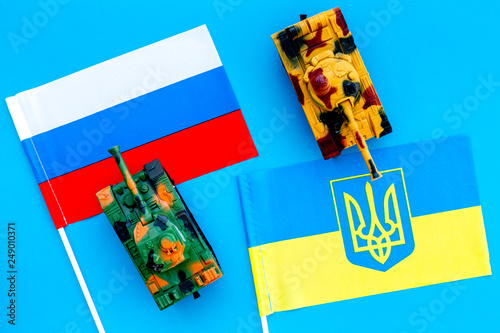 War, confrontation concept. Russia, Ukraine. Tanks toy near russian and Ukrainianflag on blue background top view photo