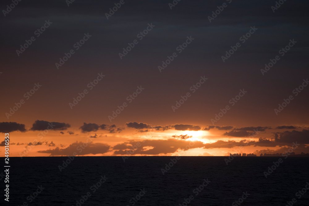 View of a vibrant sunset at dusk with the ocean in the foreground View of a vibrant sunset at dusk with the ocean in the foreground