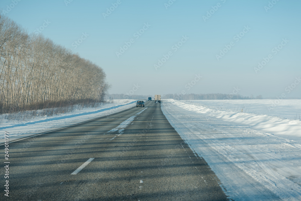 Asphalt road in winter in the forest. Asphalt under the snow. Road in the snow. Winter road.