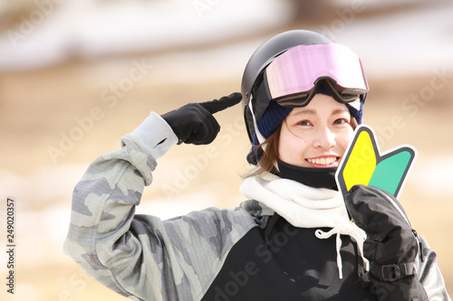 初心者マークを持ちヘルメットを指さすスノーボードウェアの女性