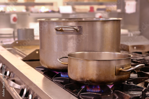 LARGE STAINLESS STEEL PANS WITH BIG HANDLES WARM UP WITH THE FLAMES OF AN INDUSTRIAL KITCHEN OF GAS
