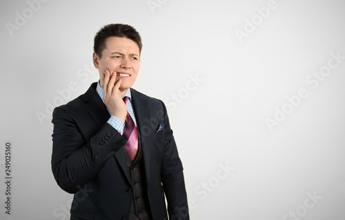 Young attractive guy businessman in suit on gray background with strong toothache.