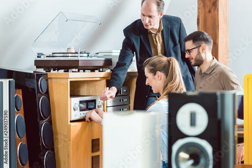 Couple testing a Hi-Fi system in the store with the salesman explaining photo