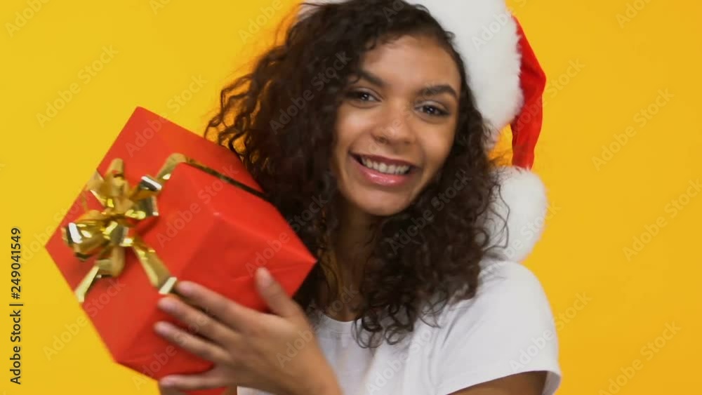 Cheerful brunette in Santa hat dancing with present, big sale before Christmas Cheerful brunette in Santa hat dancing with present, big sale before Christmas