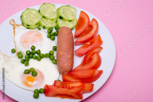 Homemade fried eggs with sausages on a white plate on a pink background. Classic breakfast. View from above.