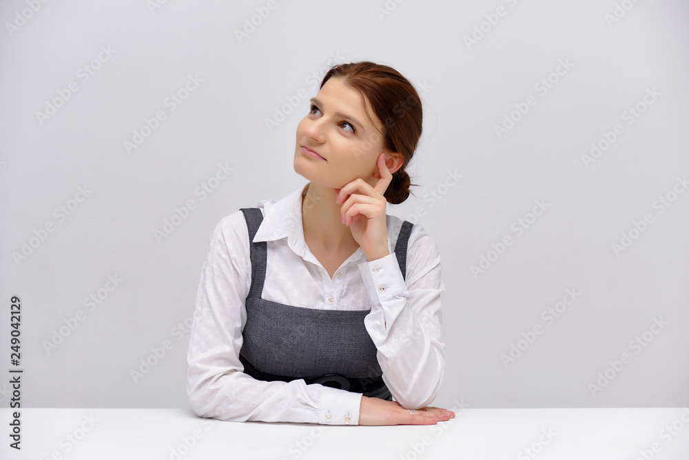 Concept studio Portrait of a young beautiful girl manager brunette sitting at a table on a white background and talking. Concept studio Portrait of a young beautiful girl manager brunette sitting at a table on a white background and talking.