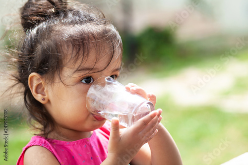 Cute child girl drinking clear water outdoors. Pure water
