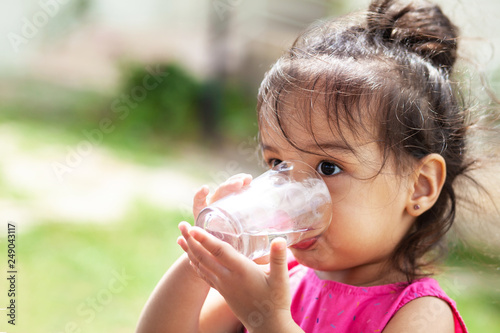 Cute child girl drinking clear water outdoors. Pure water