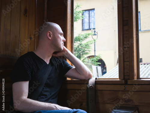 Transportation and travel concept. A handsome man with black t-shirt waiting, sitting on a train and looking outside the window.