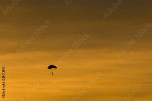 Silhouette of parachutist flying slowly on parachute in the beautiful sky at sunset.