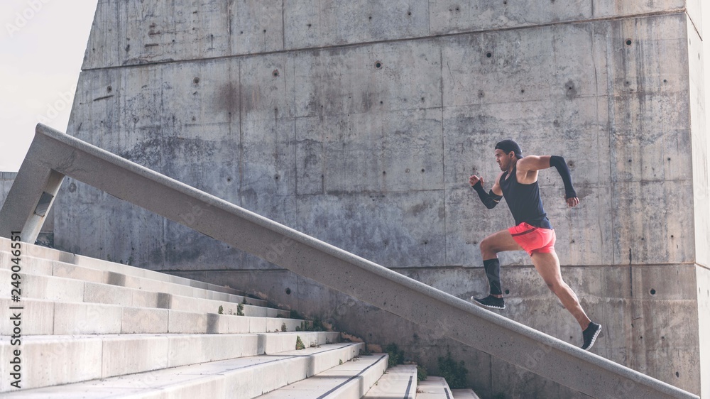 Muscular hispanic dark-skinned male athlete build running up a flight of stairs with speed.Concret background wall with copy space area for text message or advertising content