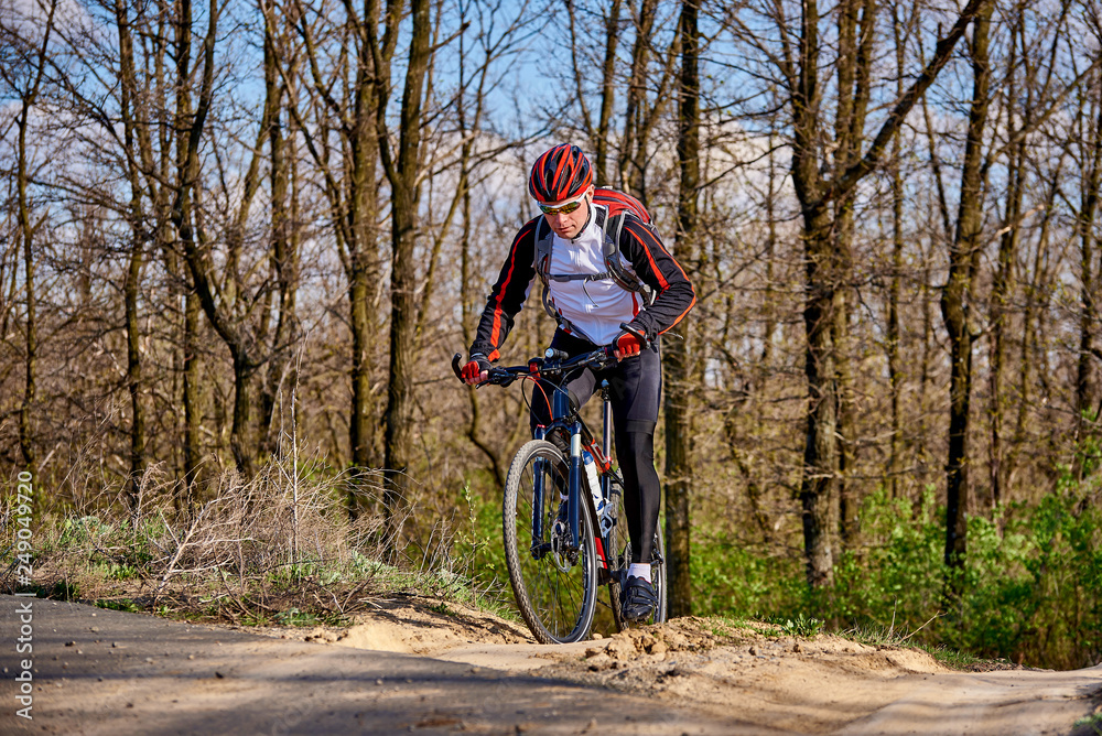 Sports cyclist rides along a trail in the forest on a spring sunny day.