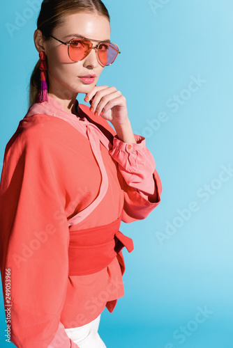 attractive woman in trendy living coral clothing and sunglasses posing isolated on blue
