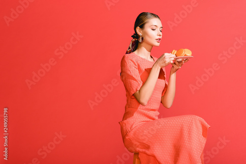 fashionable woman holding plate with macaroons isolated on living coral.  color of the year 2019 concept