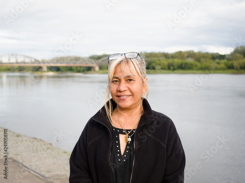 60 years old age Asian Thai woman and glasses on her head traveling in Europe old beautiful city with river landscape view on background for holiday.