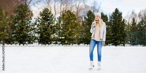 happy young woman in ice skates posing with coffee cup at rink in winter park - copy space over ice