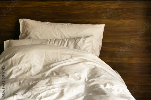 modern bedroom with fresh white linen, pillows and messy blanket on the wooden bed