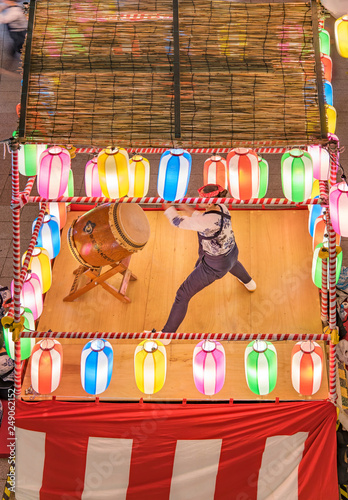 View of the square in front of the Nippori train station decorated for the Obon festival with a yagura tower illuminated with paper lanterns where a girl in traditional costume is playing taiko drum. photo