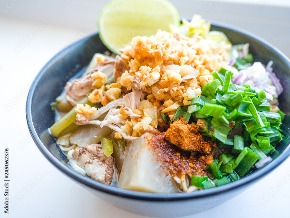 Shred chicken instant noodles with deep fried garlic. chili powder, lemon, spring onion and hot soup with spices in a bowl on white table, Thai noodles food Shred chicken instant noodles with deep fried garlic. chili powder, lemon, spring onion and hot soup with spices in a bowl on white table, Thai noodles food
