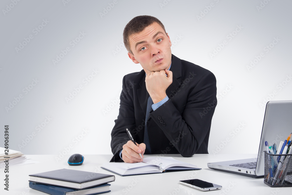  Serious businessman skeptically looking at you sitting at his desk on gray background.Human face expression