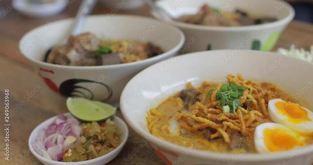 Northern Thailand noodle style called Khao-soi on the table with a hand seasoning spices into a bowl. Northern Thailand noodle style called Khao-soi on the table with a hand seasoning spices into a bowl.