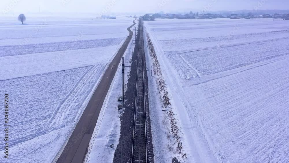 Aerial view with drone flying high over the railway over the snow covered countryside fields on a cold winter sunny day Aerial view with drone flying high over the railway over the snow covered countryside fields on a cold winter sunny day