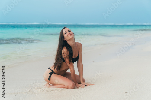Sexy brunette girl in a swimsuit sunbathes on the white sand beach.