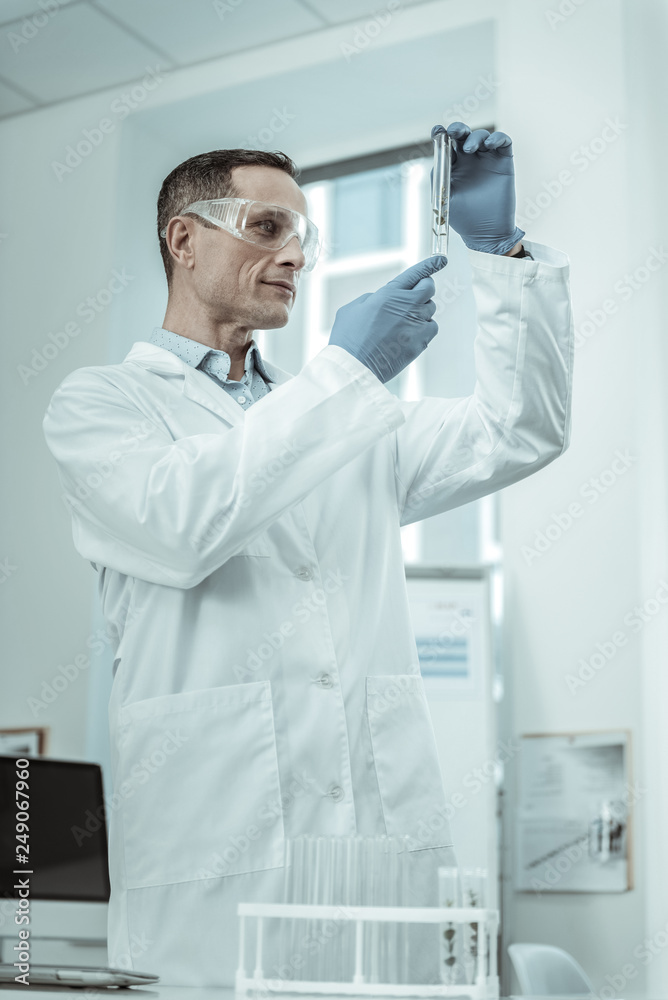 Attentive scientist in white robe and rubber gloves carrying sample Attentive scientist in white robe and rubber gloves carrying sample