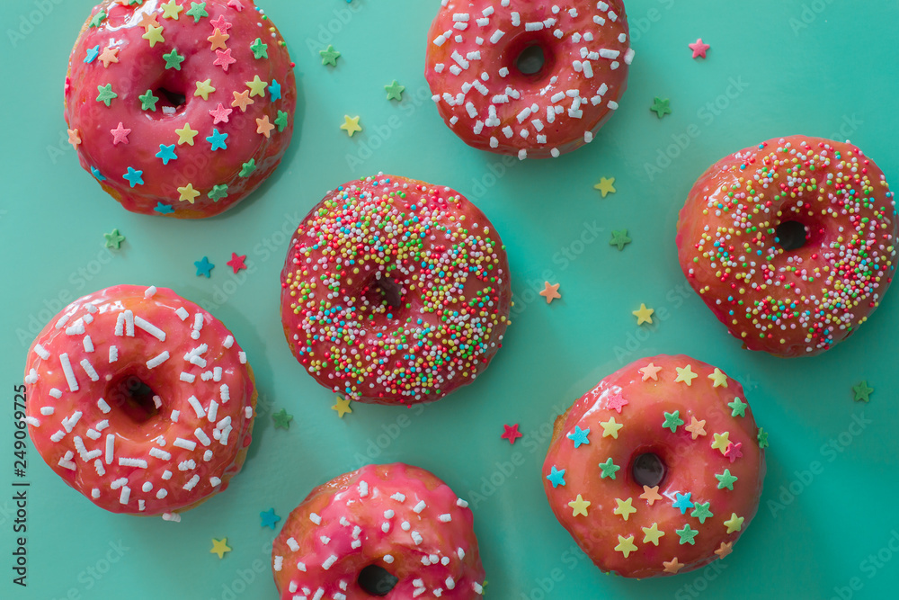 Pink glazed doughnuts with sprinkles on turquoise background Pink glazed doughnuts with sprinkles on turquoise background