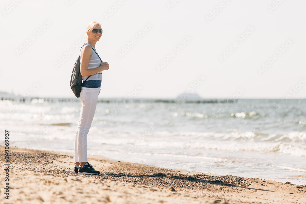 Young, beautiful blonde girl walking at the beach. Stylish woman in white pants and sunglasses near sea
